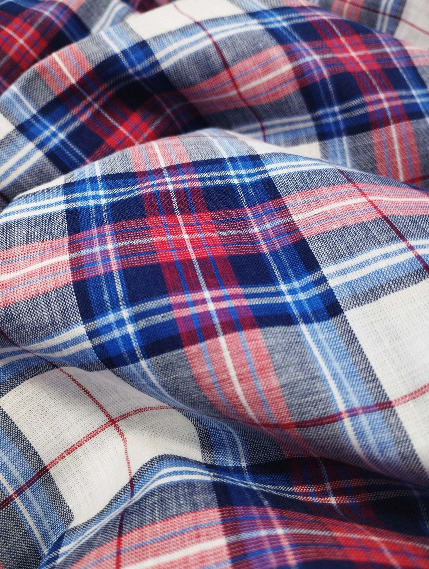 Close-up of red, blue, white, and navy plaid fabric with textured weave and folds