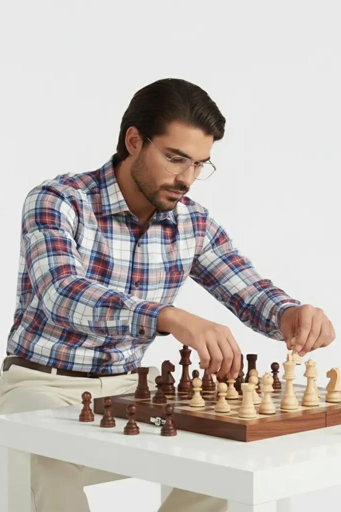 Man in plaid shirt and glasses playing chess on wooden board at white table