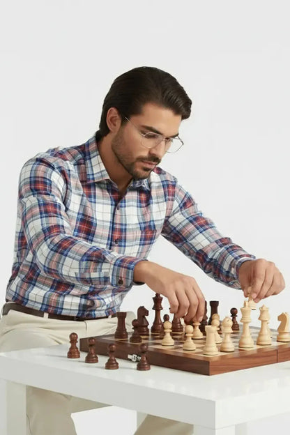Man in plaid shirt and glasses playing chess on wooden board at white table