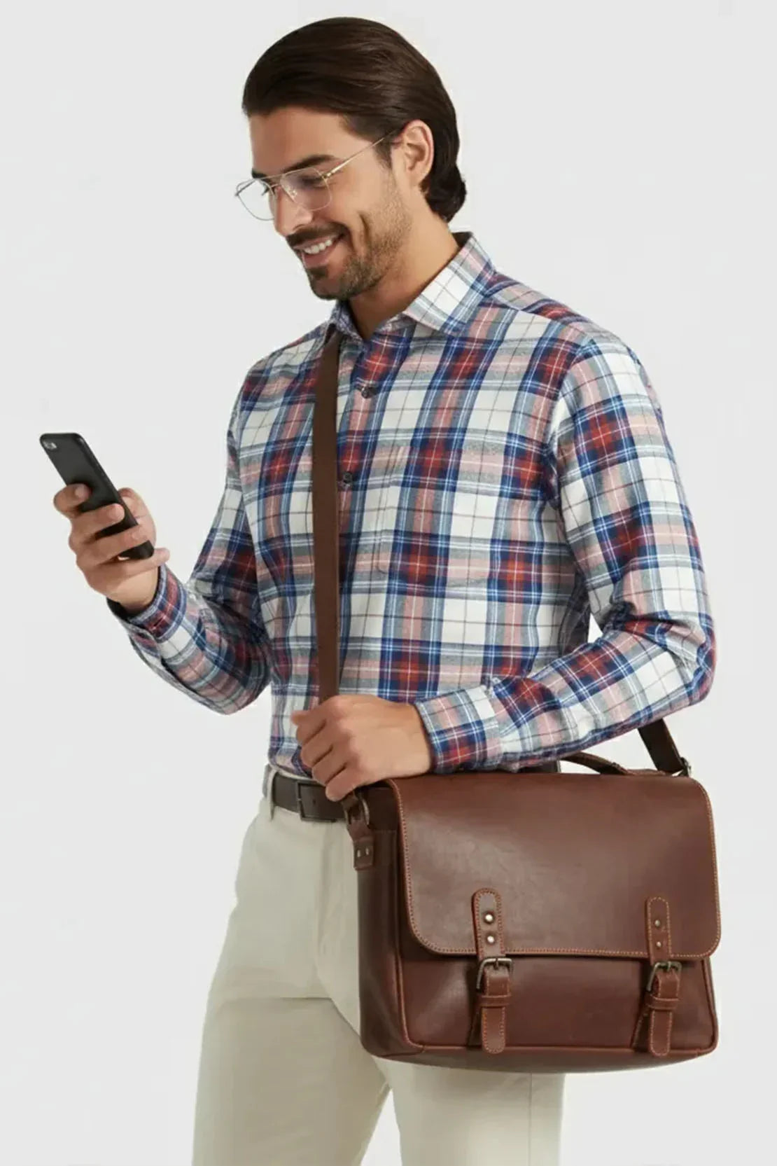 Man in plaid shirt and beige pants holding brown leather messenger bag and using smartphone