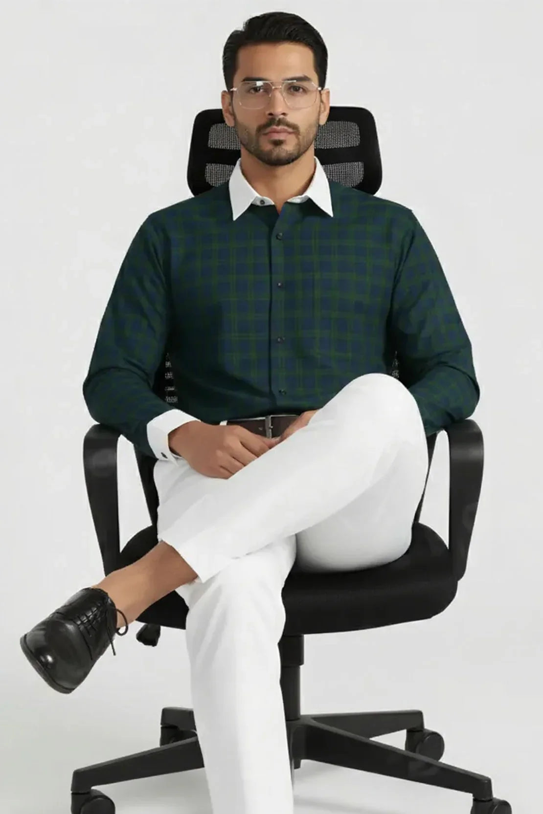 Man in green checked shirt with white collar and cuffs, white pants, black shoes, sitting on black office chair