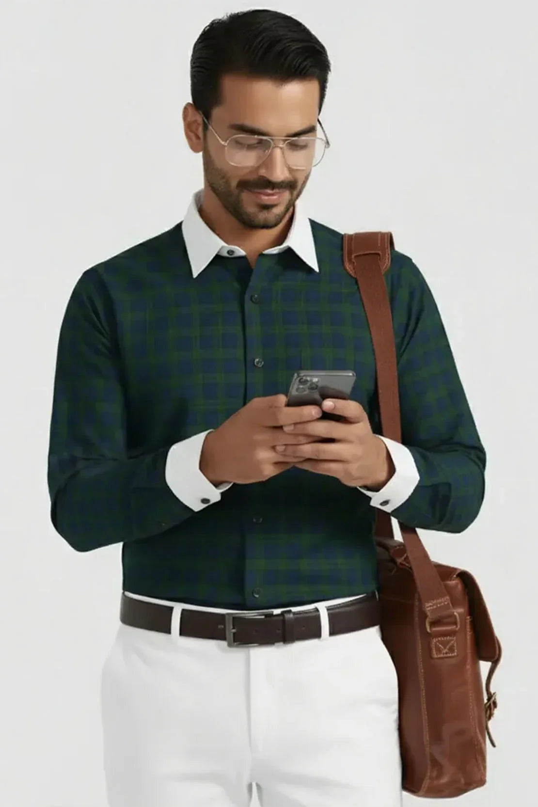 Man wearing green checkered shirt with white collar and cuffs, white pants, brown belt and brown leather shoulder bag, using smartphone